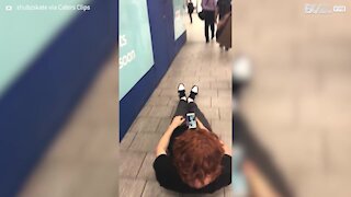 Young man rides skateboard lying down in London tube station