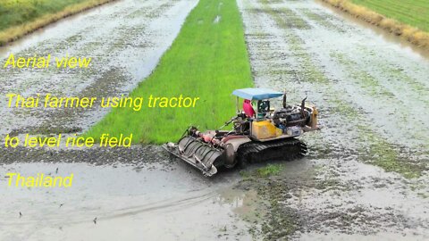 Aerial view farmer using tractor to level rice field in Thailand