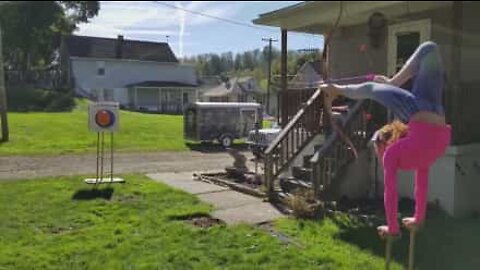 Girl pops a balloon with a bow and arrow...while doing a handstand!