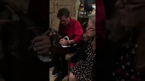 RANDY TRAVIS signs a guitar for Donna Fitzgerald Veterans For America First at his Texas home