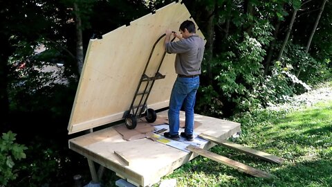 A shed like a plywood box, overhanging a slope.