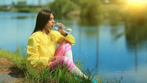 girl-sits-on-grass-near-lake-and-drinks-water full HD video