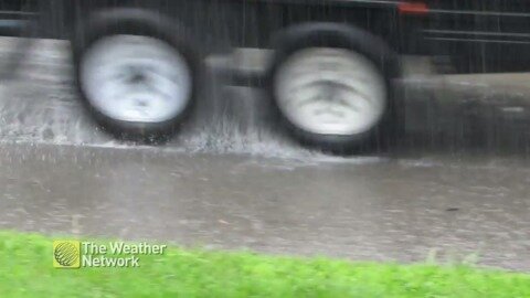 Cars drive through puddles on a rain-drenched road