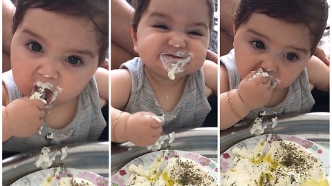 Baby girl eating yogurt by her hand