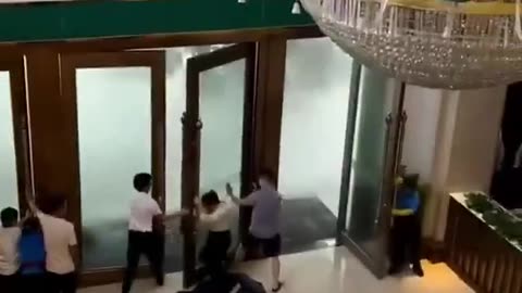 Hotel workers try to hold open doors hit by powerful gusts of wind from super typhoon.