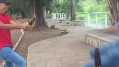 Red shirt guy holding bottle for guy to kick cap off kicking guy falls after missing bottle