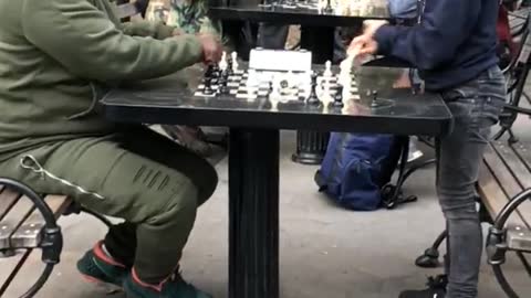 Little boy playing chess in park against man in green track suit