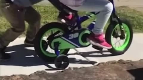 Little boy helps friend ride a bike.