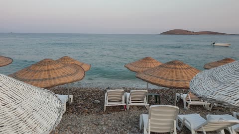 Lines Of Beach Chairs Shaded By Rattan Umbrellas On The Shore Of A Beach