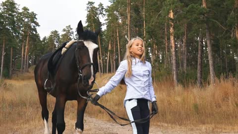 the little girl walks in autumn forest together with horse