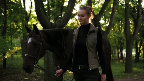 Slowmotion shot of attractive young female jokey walking with brown horse