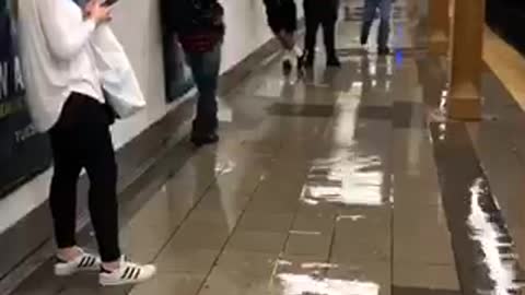 Floor leaking subway station platform guy trying to block hole with foot