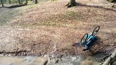 Blue/green sweater boy tries to jump creek in woods but goes over handlebars