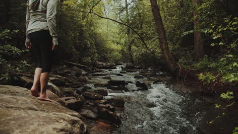 A Woman Walking Barefooted On The Riverside Rocks