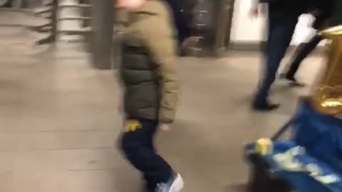 Little boy in green dancing next to street performer