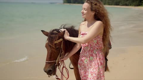 Pleasant free woman and brown horse walking on seaside in light windy day