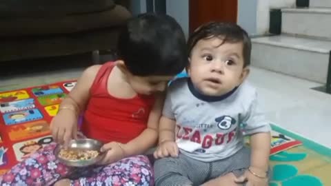 Cute Girl trying to feed her cute brother