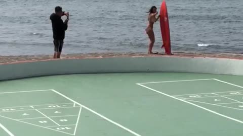 Woman in bathing suite poses for picture next to surf board