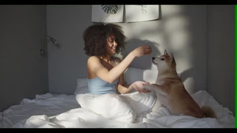 Woman Teasing Her Dog With Food While In Bed