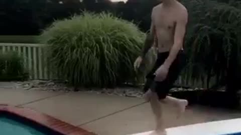 Guy in black swim trunks belly flops off diving board into pool