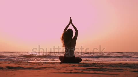 Woman meditating on the beach during sunrise