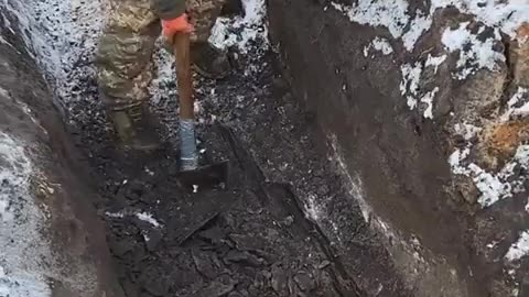 Ukrainian soldier using an axe to dig a trench