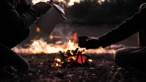 People pouring hot drinks around a campfire