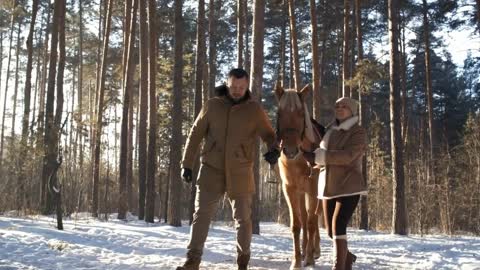 Happy couple holding leading reins, smiling and chatting while walking towards the camera with horse