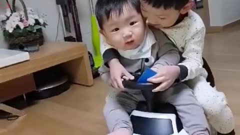 Two brothers riding a toy car together.