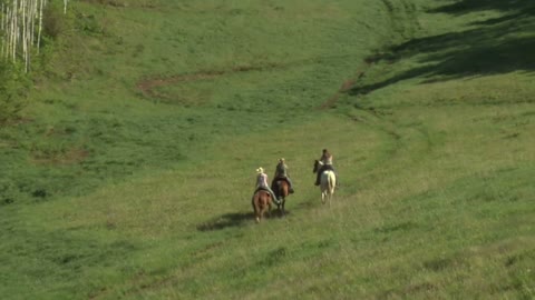 Three Young Women On Horses Ride Across Green Meadow- Zoom Out