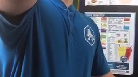 Male worker in a blue shirt at a fast food window chugs a beer