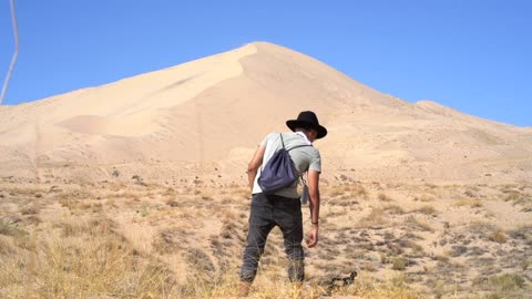 Back View Of A Man Holding A Camera Standing In Front Of A Sand Dune In The Dessert