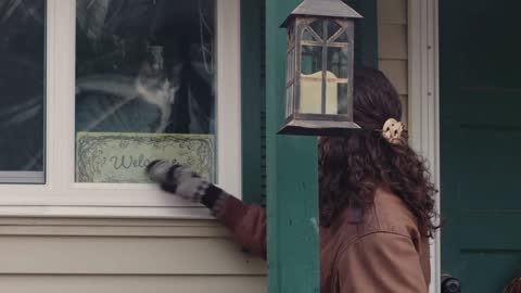 Young woman on her front porch plays with her cat which is staring from window