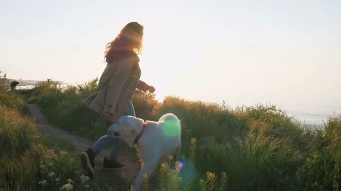 Young girl teasing retriever dog on the path near the sea at sunset