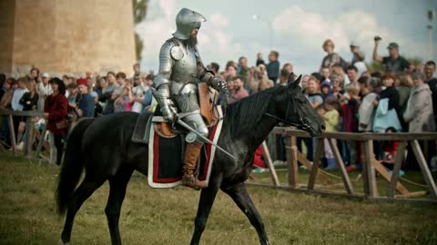 A man knight with opened helmet riding a horse around the battlefield