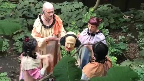 Four people in the forest doing prayers around decapitated head sculpture with headphones