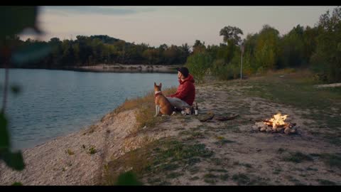 Man and his best friend, brown basenji puppy dog sit on sea or lake shore