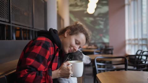 Side view of young woman drinking coffee and hugging and kissing her brown and white adorable dog