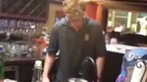 Guy wearing polo takes swing from clear bottle then drops it in bar