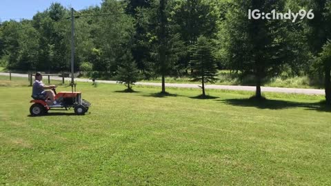 Two guys racing on lawn mowers one flips over