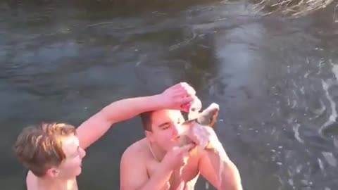 Two guys in river one drinks beer through fish