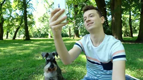 Boy having a videocall on smartphone while relaxing in the park with his dog