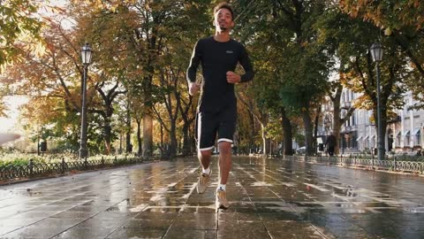 Young black man running with his white labrador dog through the city park during