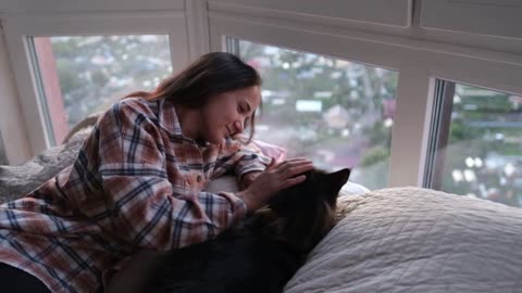 Young beautiful brunette woman lying on the bed by the window stroking a maine coon cat