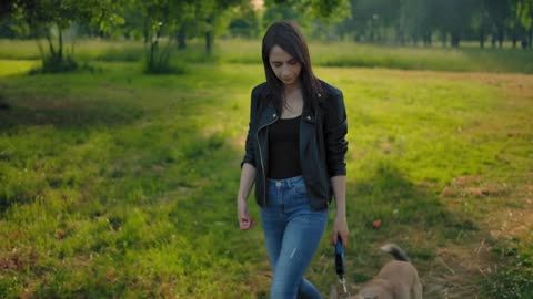 Frontal wide view of a young woman in jeans and leather jacket leading her dog for a walk