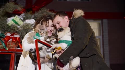 Happy couple holding pets on hands on Christmas evening decoration background outdoor