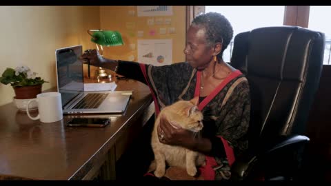 African American woman trying to work with an orange cat in her lap writing sticky note reminders