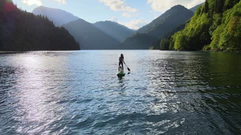 Aerial drone view of pretty fit woman paddle on sup board at mountain lake during sunset