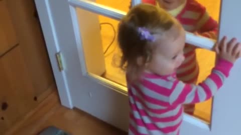 Twin babies giggle at each other through glass doors