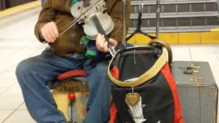 Old man plays violin and cajon box in front of subway escalators